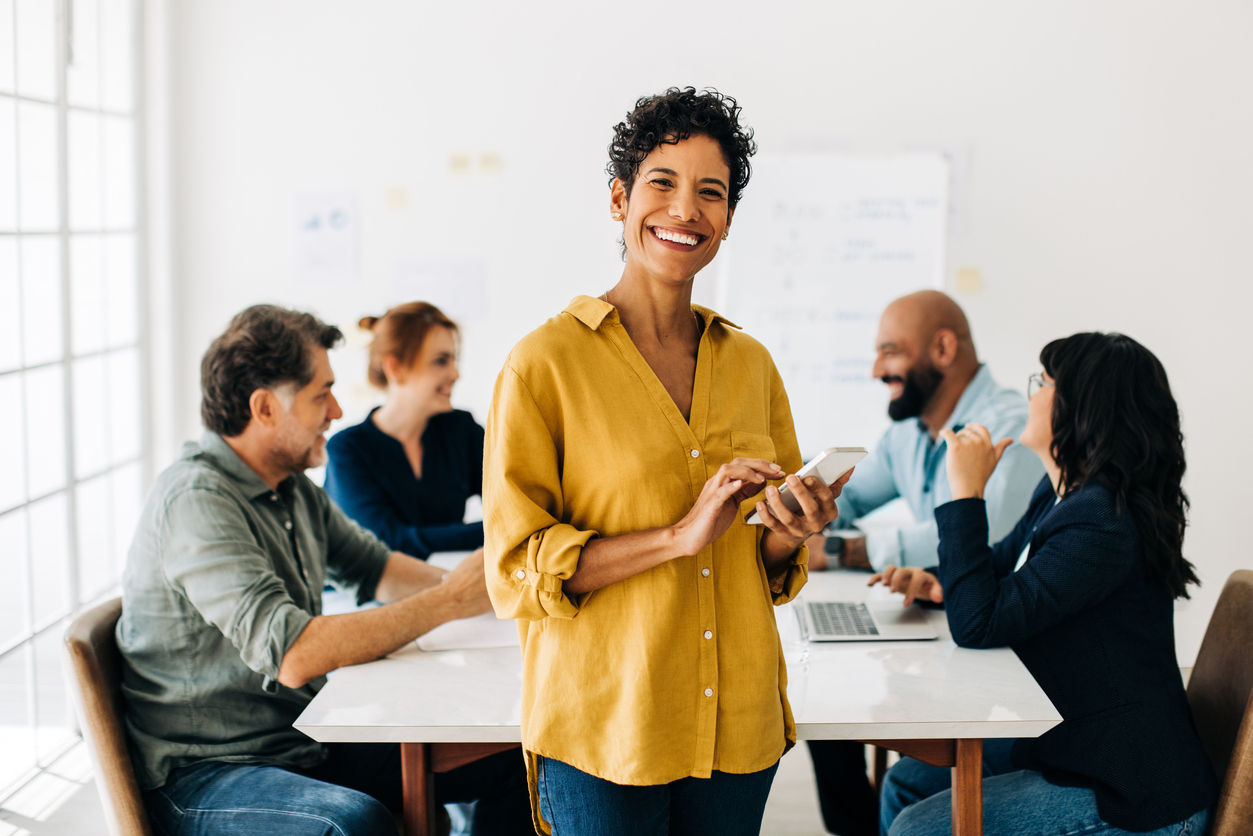 woman smiling while she sits at a conference table with colleagues 